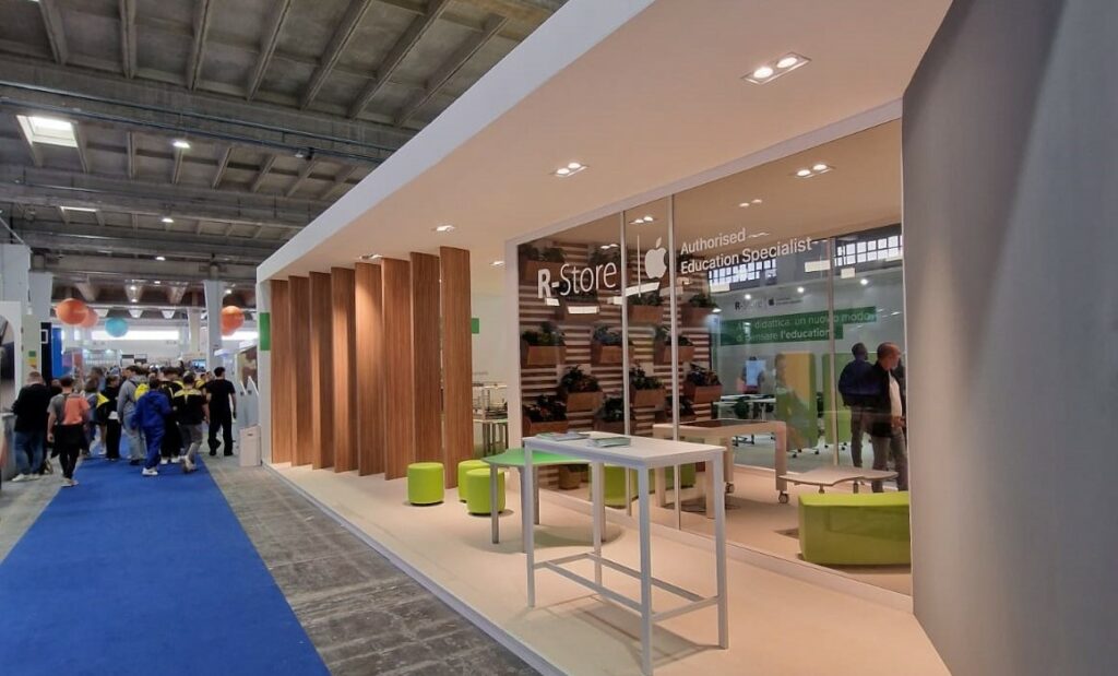 stand R-Store Didacta 2024 - Area espositiva con arredi moderni, postazioni tecnologiche e installazioni verdi integrate nell'allestimento fieristico