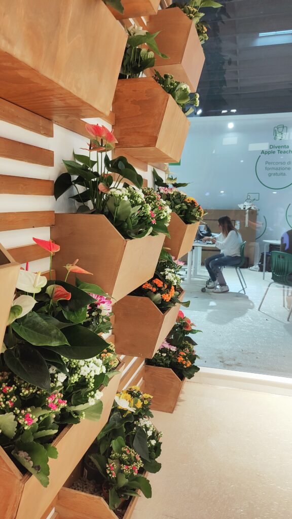 Allestimento verde dello stand R-Store a Didacta 2024 - Composizioni floreali integrate con postazioni di lavoro, perfetta fusione tra natura e spazio operativo fieristico